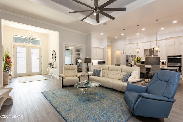 living room with ceiling fan with notable chandelier, light hardwood / wood-style floors, crown molding, and french doors