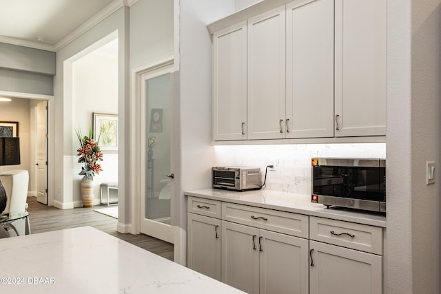 kitchen with white cabinetry, light stone counters, crown molding, and light wood-type flooring