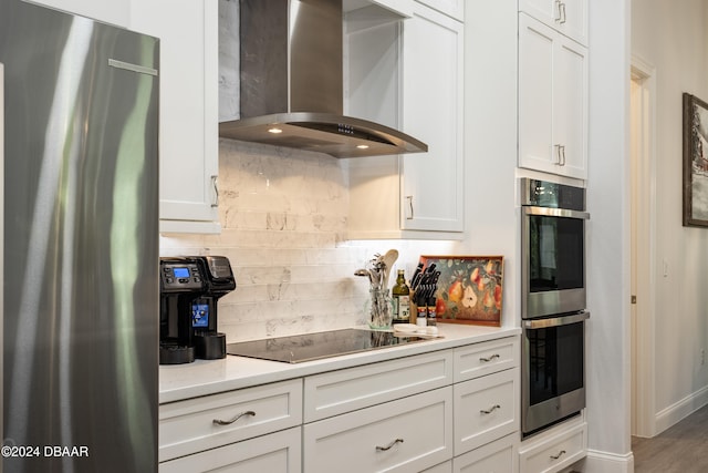 kitchen featuring white cabinetry, wall chimney range hood, wood-type flooring, decorative backsplash, and appliances with stainless steel finishes