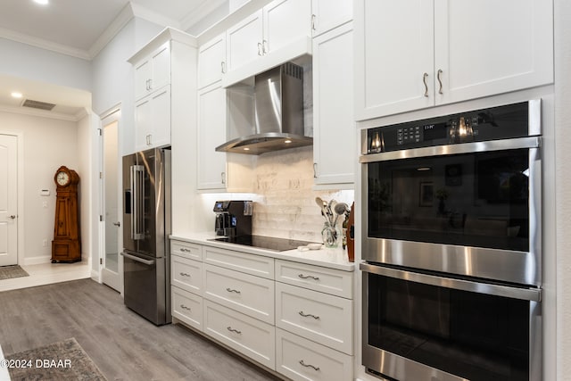 kitchen with wall chimney exhaust hood, ornamental molding, light hardwood / wood-style floors, white cabinetry, and stainless steel appliances