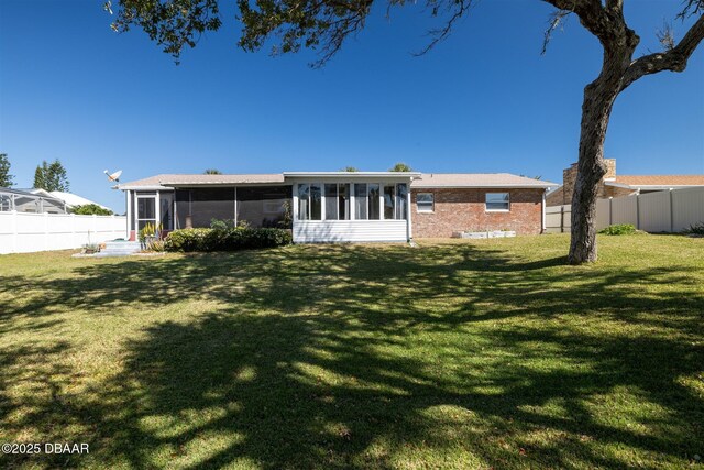 rear view of property featuring a yard, brick siding, a fenced backyard, and a sunroom