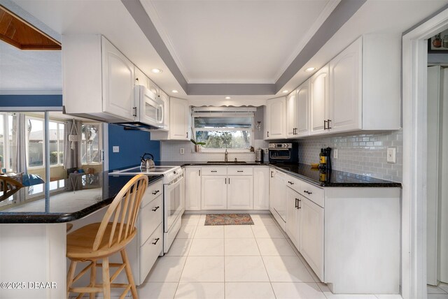 kitchen with a peninsula, white cabinets, white appliances, a raised ceiling, and a sink