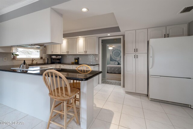 kitchen featuring visible vents, freestanding refrigerator, dark countertops, a kitchen breakfast bar, and tasteful backsplash