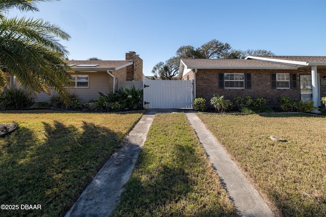 view of front facade with brick siding, fence, a front yard, and a gate