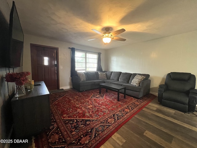 living room featuring baseboards, a ceiling fan, and dark wood-style flooring