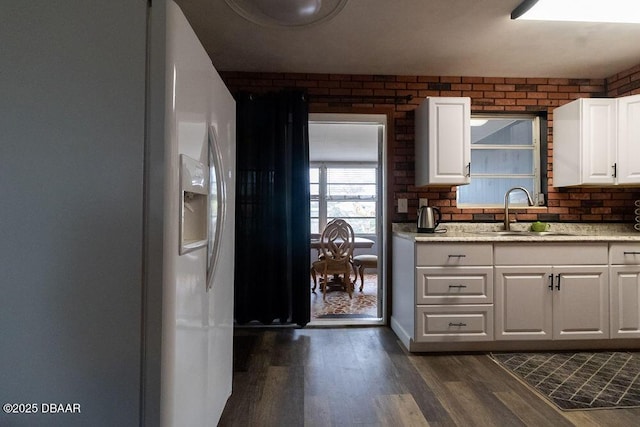 kitchen with brick wall, white refrigerator with ice dispenser, dark wood-style flooring, a sink, and white cabinetry