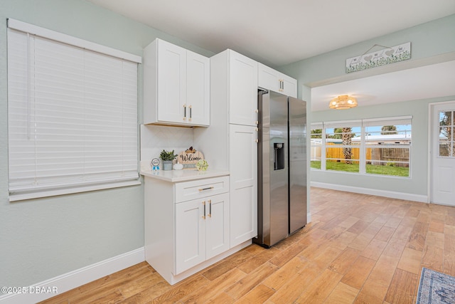 kitchen featuring stainless steel fridge, light wood-type flooring, and white cabinetry