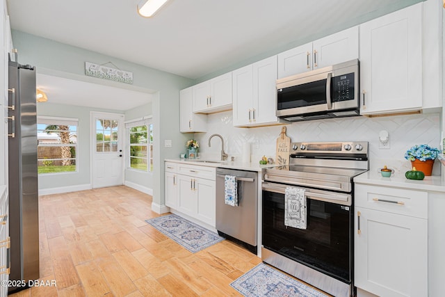 kitchen with appliances with stainless steel finishes, light wood-type flooring, backsplash, sink, and white cabinetry