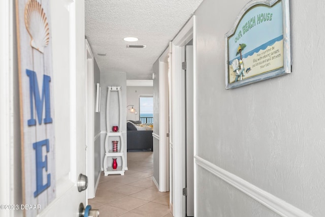 hallway with a textured ceiling and light tile patterned floors