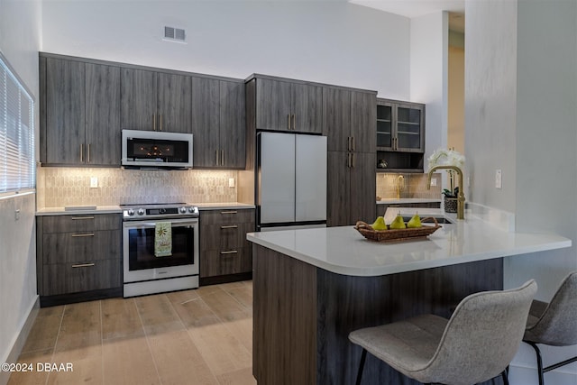 kitchen with stainless steel appliances, a breakfast bar, kitchen peninsula, backsplash, and light wood-type flooring