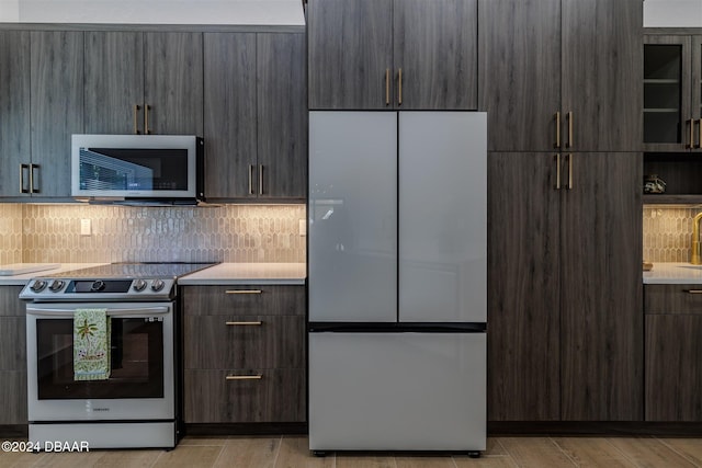 kitchen featuring light wood-type flooring, appliances with stainless steel finishes, decorative backsplash, and dark brown cabinetry