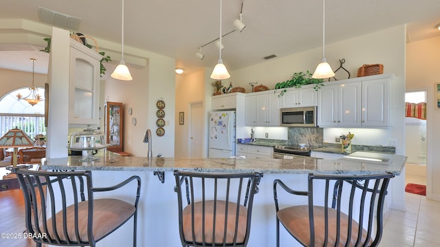 kitchen featuring white cabinetry, tasteful backsplash, light stone counters, pendant lighting, and stainless steel appliances