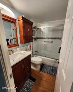 full bathroom featuring toilet, vanity, hardwood / wood-style floors, and enclosed tub / shower combo