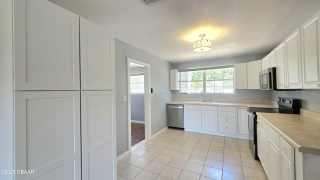 kitchen featuring a sink, stainless steel appliances, light tile patterned floors, baseboards, and white cabinets