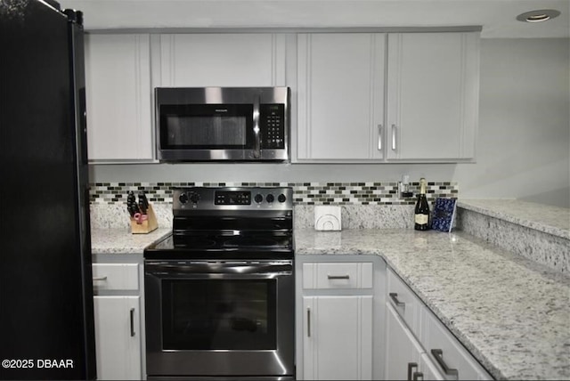 kitchen with black fridge, electric range oven, white cabinets, and decorative backsplash