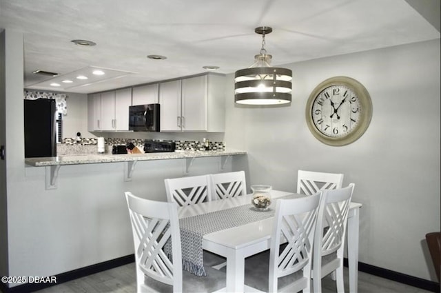 kitchen featuring decorative light fixtures, stainless steel fridge, kitchen peninsula, light stone countertops, and white cabinets