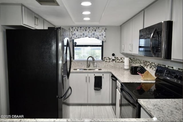 kitchen featuring sink, white cabinetry, light stone counters, tasteful backsplash, and black appliances