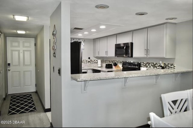 kitchen with tasteful backsplash, light stone countertops, a kitchen bar, black / electric stove, and kitchen peninsula