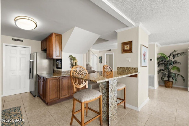 901 S Atlantic Ave Unit 202, Ormond Beach, FL 32176 - kitchen featuring brown cabinetry, a kitchen breakfast bar, light tile patterned floors, a textured ceiling, and stainless steel fridge
