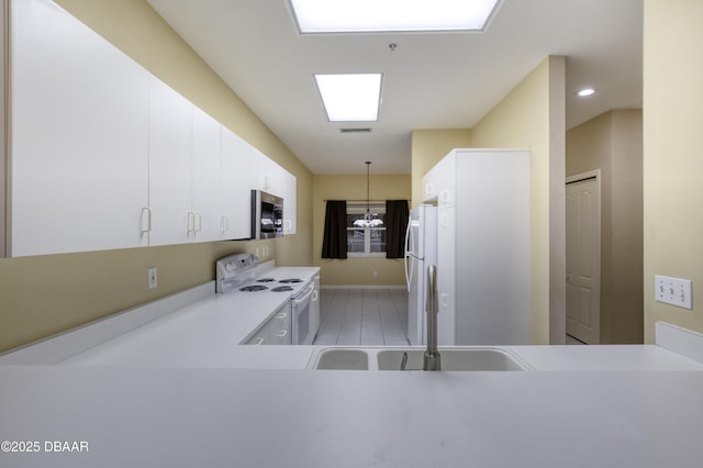 kitchen with a chandelier, kitchen peninsula, pendant lighting, white appliances, and white cabinets