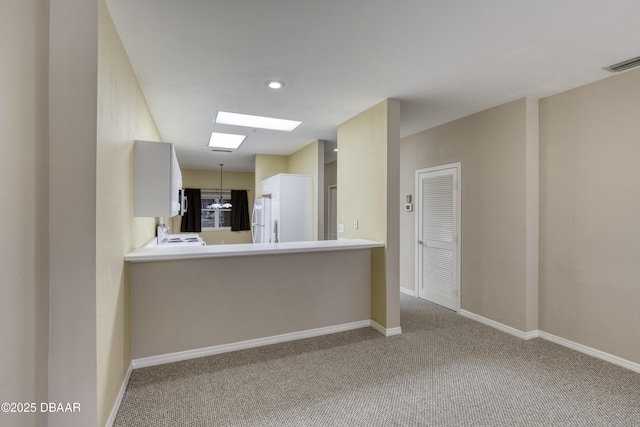 kitchen featuring white refrigerator, light colored carpet, kitchen peninsula, and a skylight