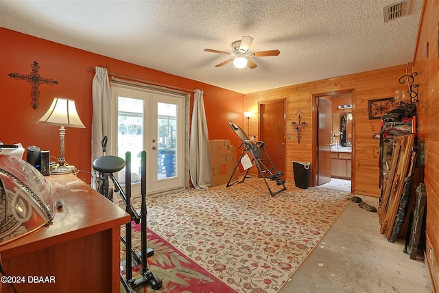 office space with a textured ceiling, french doors, wooden walls, and ceiling fan