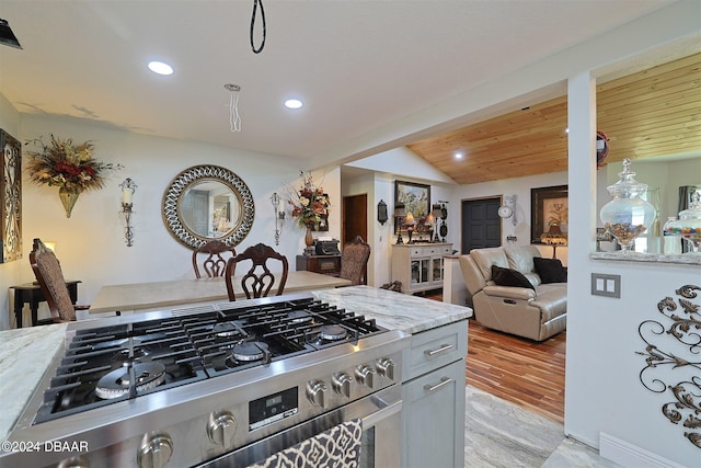 kitchen with stainless steel stove, light hardwood / wood-style flooring, light stone counters, and vaulted ceiling