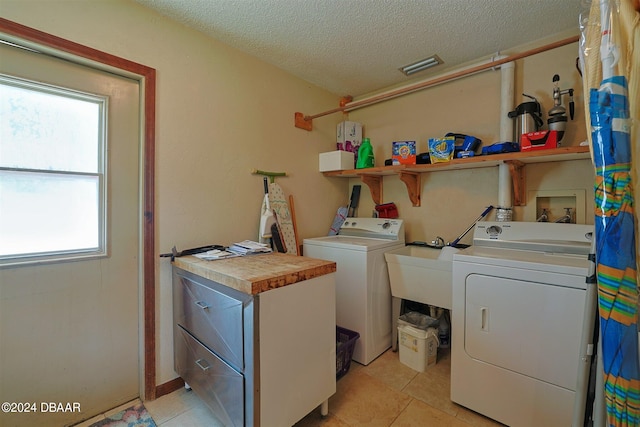 clothes washing area with a wealth of natural light, washing machine and clothes dryer, light tile patterned floors, and a textured ceiling