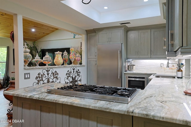 kitchen with stainless steel appliances, hardwood / wood-style flooring, sink, light stone counters, and vaulted ceiling