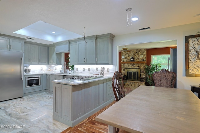 kitchen featuring a fireplace, appliances with stainless steel finishes, kitchen peninsula, and gray cabinetry