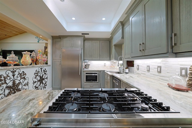 kitchen with decorative backsplash, stainless steel appliances, sink, and light stone countertops