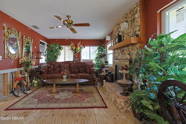 living room with ceiling fan, wood-type flooring, a textured ceiling, and a stone fireplace