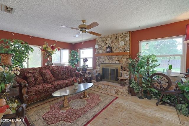 living room featuring ceiling fan, light hardwood / wood-style floors, a stone fireplace, and a textured ceiling