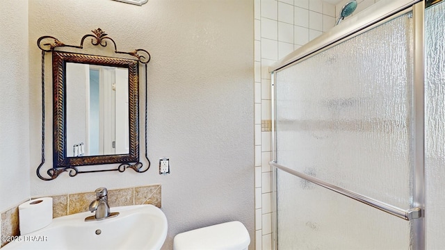 full bath with a textured wall, a stall shower, a sink, and toilet