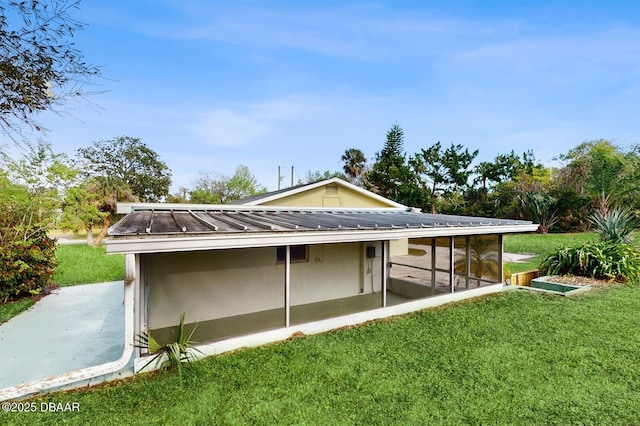 exterior space featuring a sunroom, stucco siding, a lawn, and metal roof