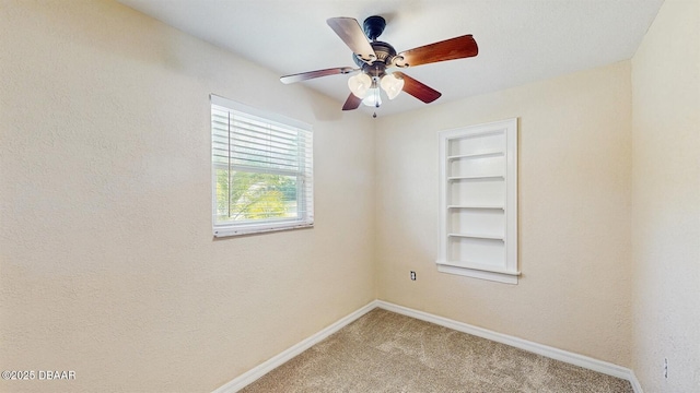 spare room with built in shelves, carpet, a ceiling fan, and baseboards