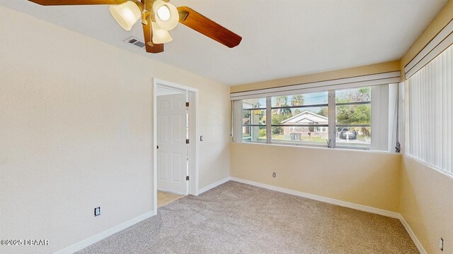 empty room with baseboards, visible vents, ceiling fan, and light colored carpet