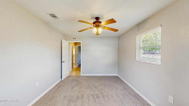 spare room with light colored carpet, visible vents, ceiling fan, and baseboards