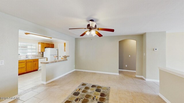 empty room featuring light tile patterned floors, baseboards, arched walkways, and a ceiling fan