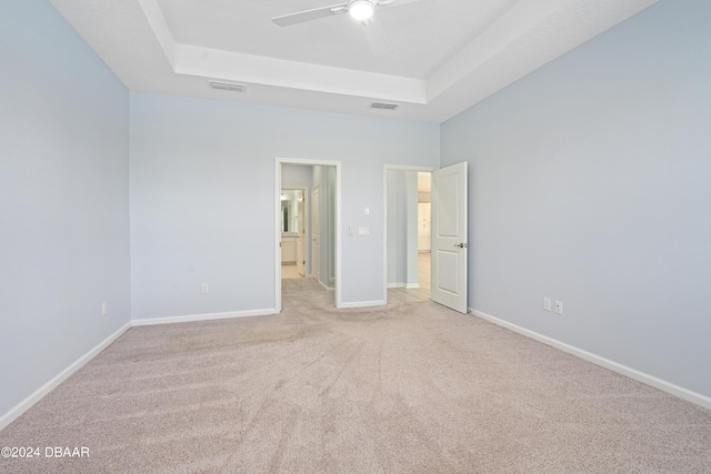 unfurnished bedroom with connected bathroom, light colored carpet, visible vents, baseboards, and a raised ceiling