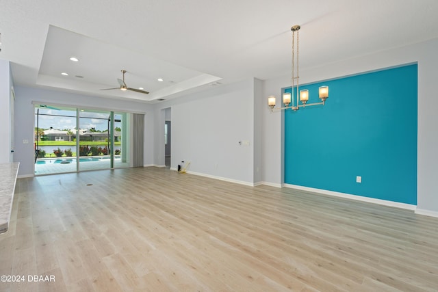 unfurnished living room with recessed lighting, ceiling fan with notable chandelier, baseboards, light wood-style floors, and a raised ceiling