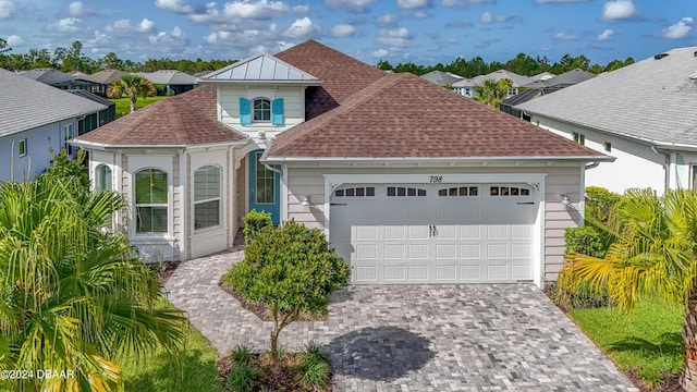 view of front of home with decorative driveway, roof with shingles, and an attached garage