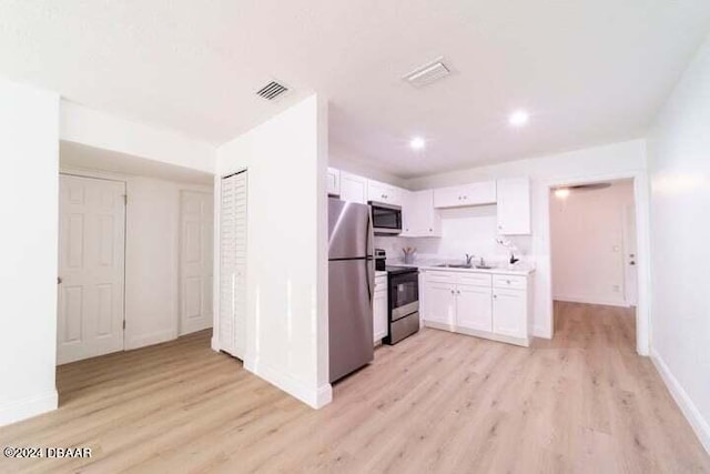 kitchen with stainless steel appliances, sink, white cabinets, light wood-type flooring, and decorative backsplash