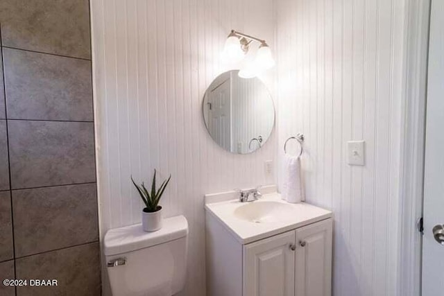 bathroom featuring vanity, wooden walls, and toilet