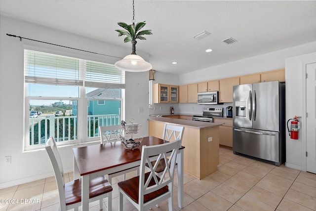 kitchen with a center island, light brown cabinets, a textured ceiling, appliances with stainless steel finishes, and decorative light fixtures