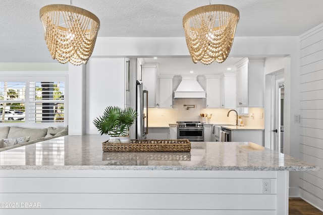 kitchen with premium range hood, decorative light fixtures, high end appliances, light stone countertops, and an inviting chandelier