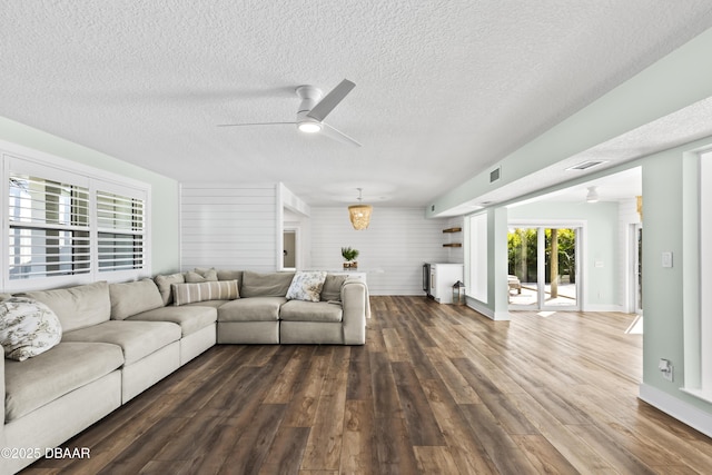 living room with dark wood-type flooring, ceiling fan, wooden walls, and a textured ceiling