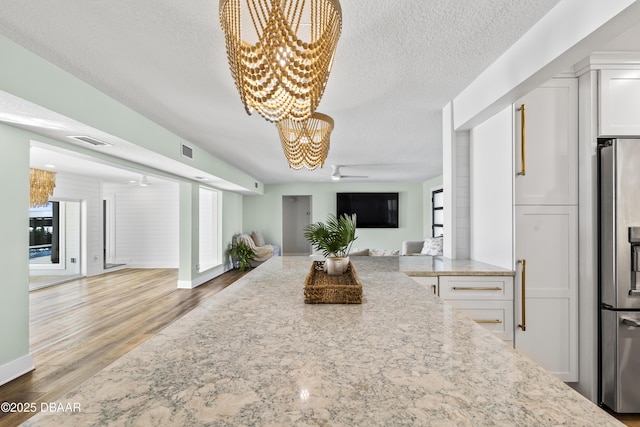 kitchen featuring hardwood / wood-style floors, white cabinetry, light stone counters, stainless steel fridge with ice dispenser, and a textured ceiling