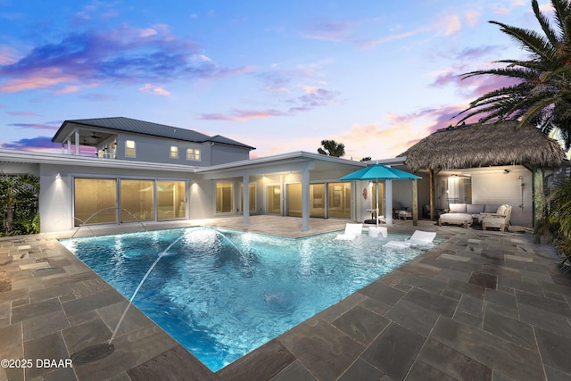 pool at dusk featuring pool water feature, an outdoor living space, and a patio