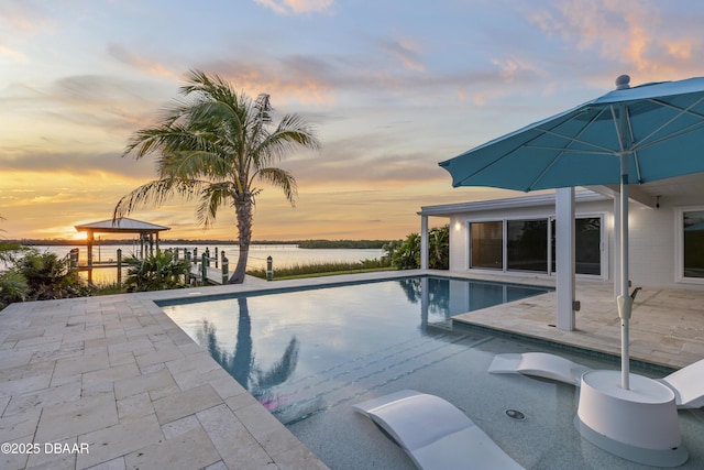 pool at dusk featuring a patio area and a water view